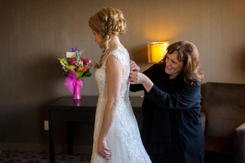 mother helping bride with wedding dress