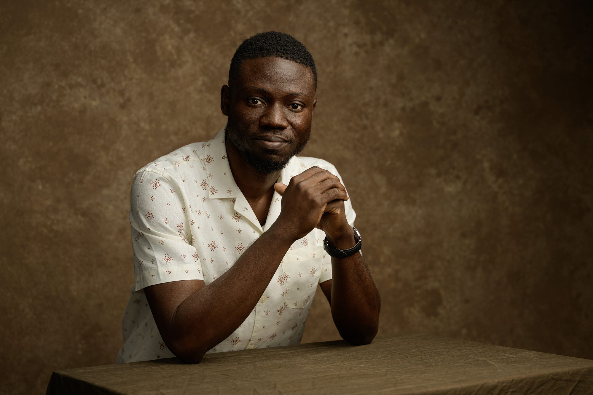Portrait of a young male sitting at a table. Brown textured background and earthy tones.
